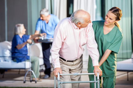 Happy female caretaker assisting senior man in using Zimmer frame at nursing home yard